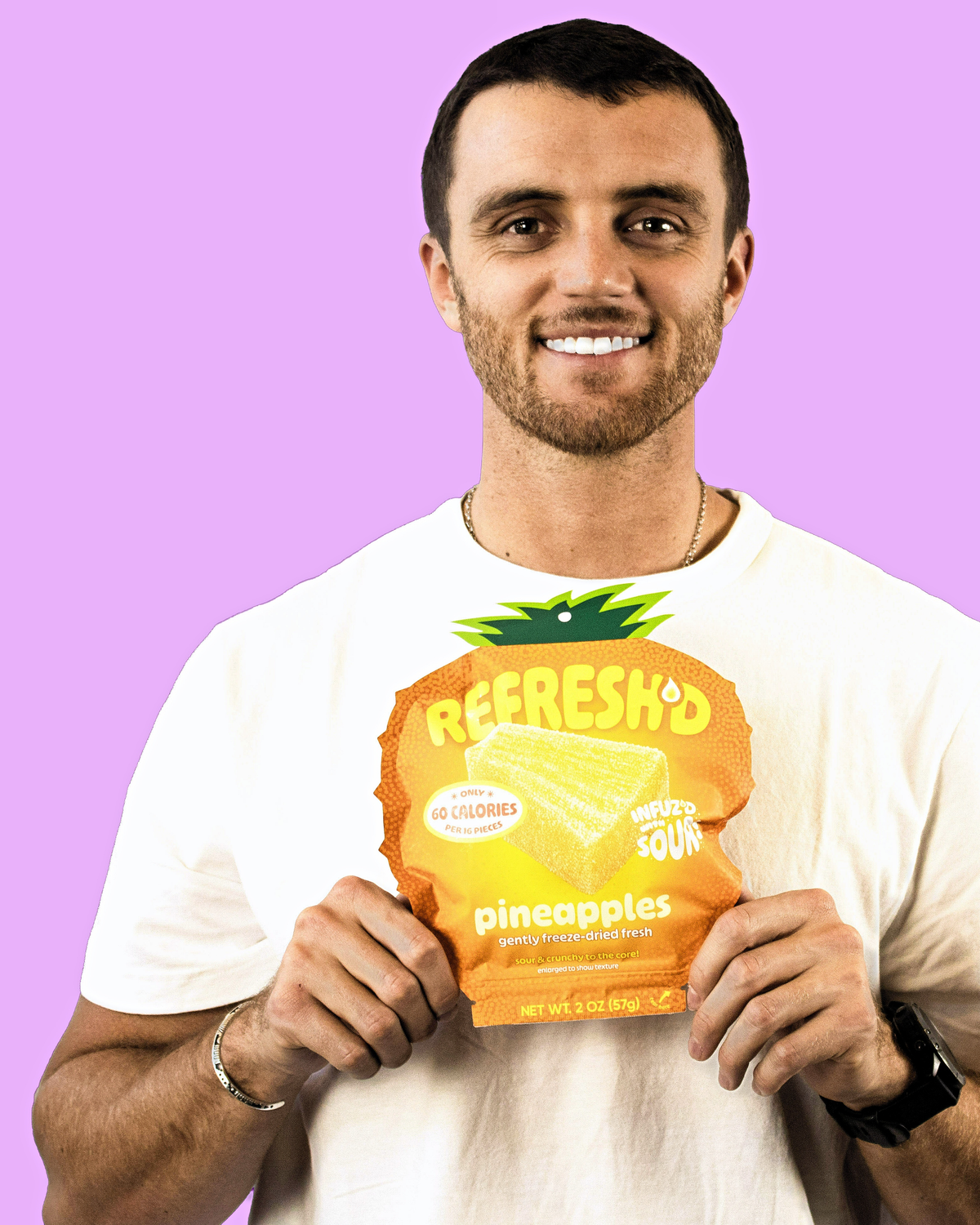 A man in a white tee holding a REFRESH'D pineapples pouch in front of a lilac background