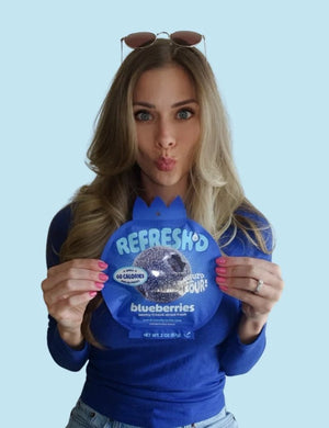 Woman holding a pouch of REFRESH'D sour freeze-dried blueberries in both hands against a pale blue wall