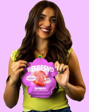 Woman holding an open pouch of REFRESH'D sour freeze-dried grapes against a lilac wall