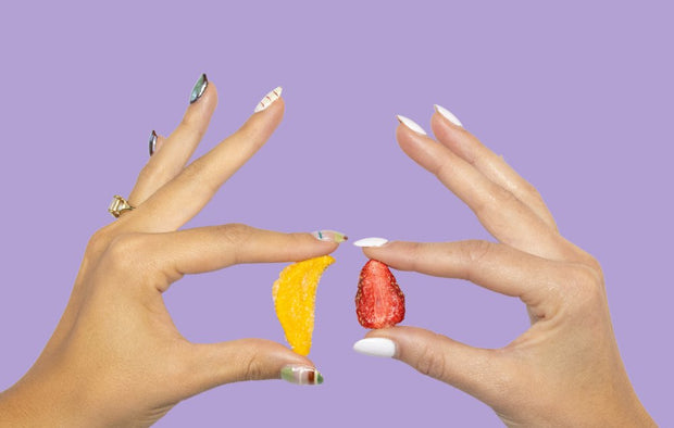 Two hands pinching a sour freeze-dried mango piece and a sour freeze-dried strawberry piece