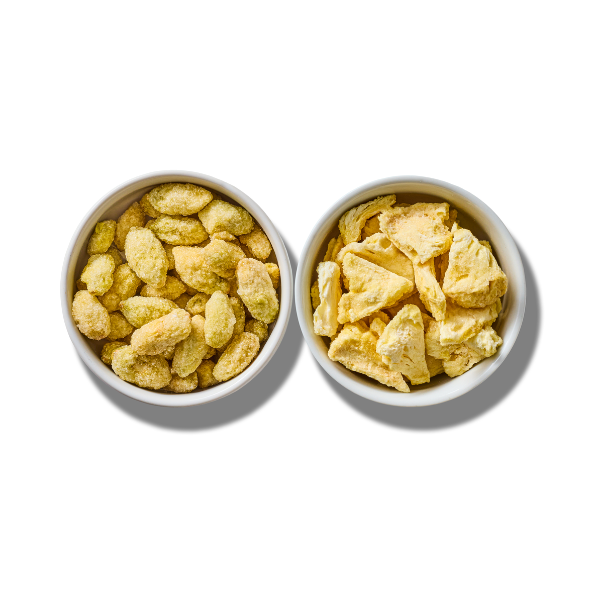 Super Sour Blend two-pack: a white bowl of freeze-dried grapes beside a white bowl of freeze-dried pineapple pieces, seen from above on white