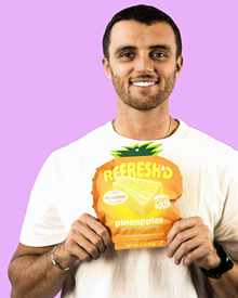 A man in a white tee holding a REFRESH'D pineapples pouch in front of a lilac background