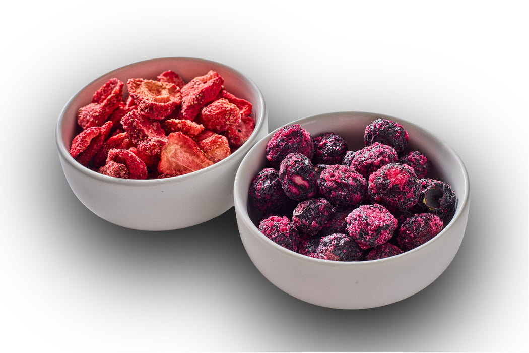 Two white bowls of sour freeze-dried strawberries and blueberries on a white background