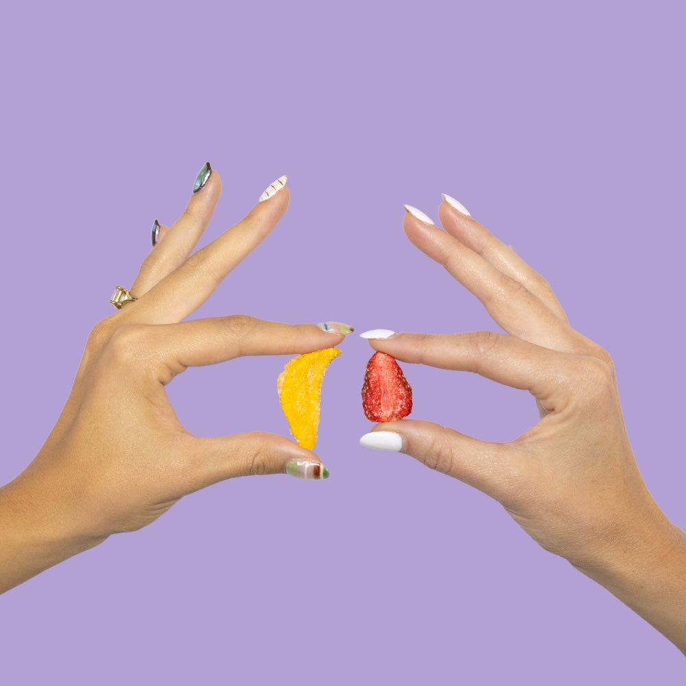 A strawberry piece and a mango piece held up, sour freeze-dried strawberries