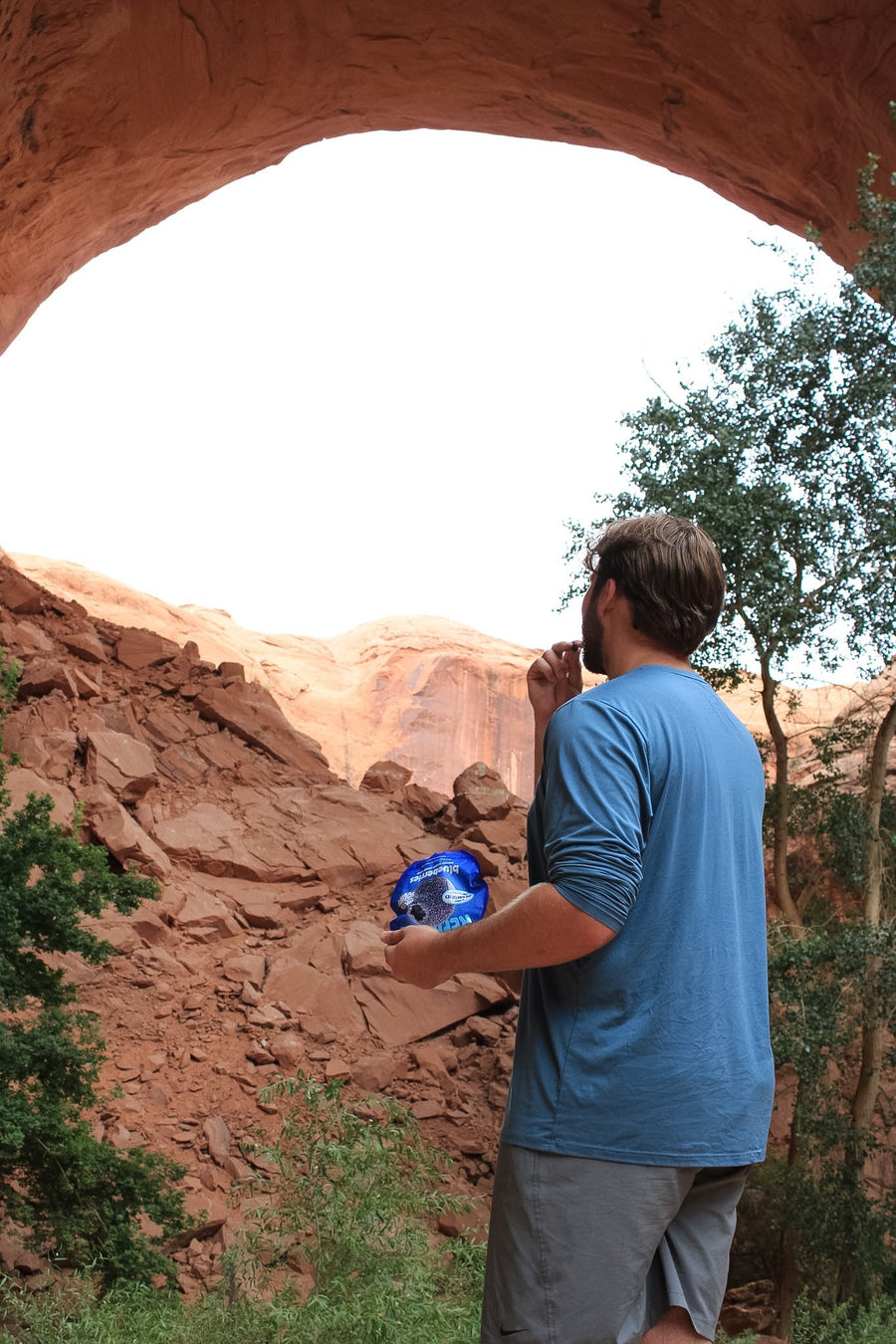A hiker standing in a sandstone arch holding a blueberries pouch