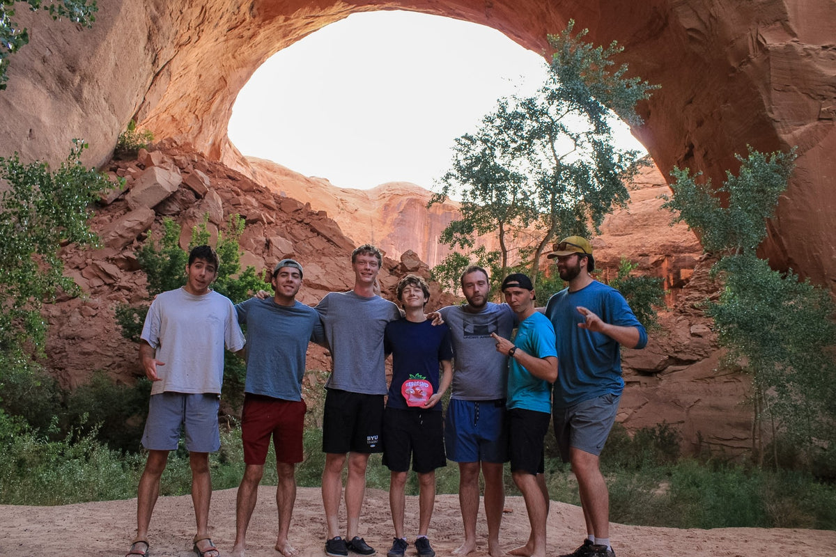 Five hikers under a sandstone arch, one holding a strawberries pouch