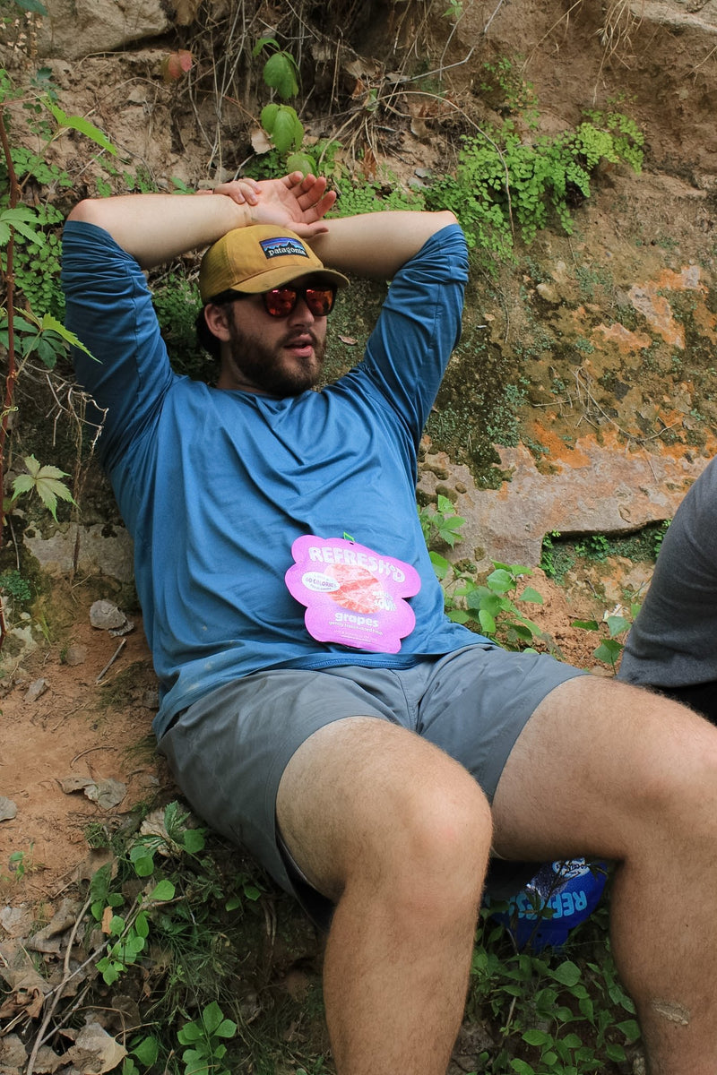 A hiker lying back in the grass with a strawberries pouch on his chest
