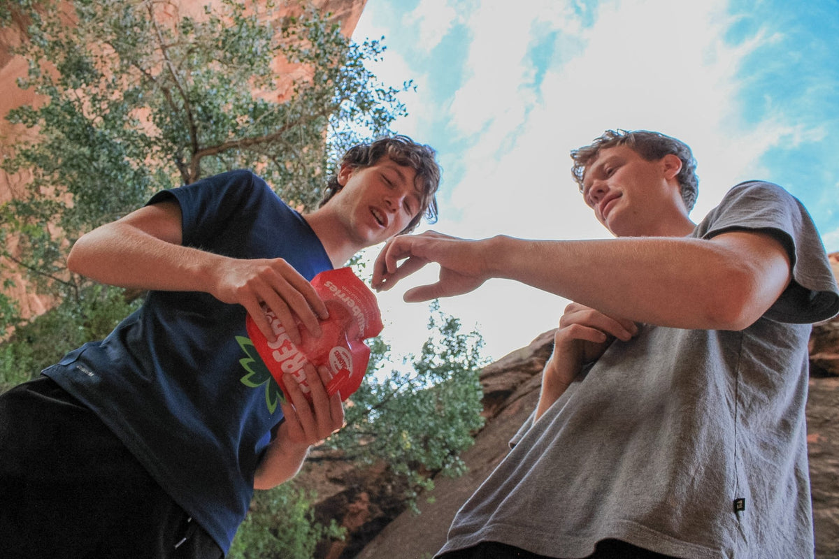 Two hikers passing a strawberries pouch under a blue sky