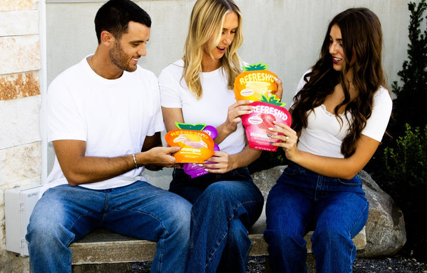 Three friends on a bench outdoors with pouches of REFRESH'D sour freeze-dried fruit