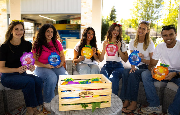 Six friends on a patio sofa around a REFRESH'D crate, each holding a pouch of sour freeze-dried fruit