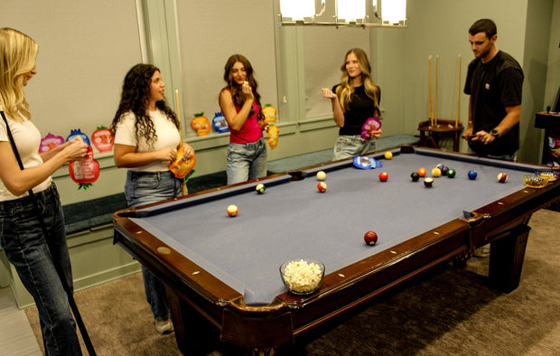 Friends around a pool table holding pouches of REFRESH'D sour freeze-dried fruit